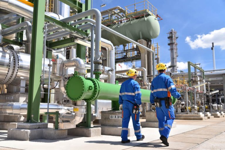 Two engineers walking past large industrial pipes.